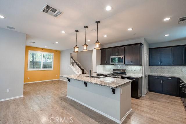 24189 Darmera Dr, Lake Elsinore, CA 92532 - kitchen featuring stainless steel appliances, a sink, a breakfast bar, light stone counters, and decorative backsplash