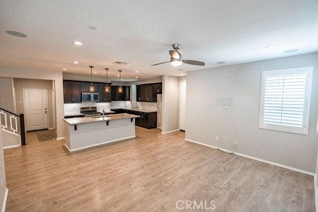 24189 Darmera Dr, Lake Elsinore, CA 92532 - kitchen with stainless steel microwave, stove, a ceiling fan, an island with sink, and light wood-type flooring