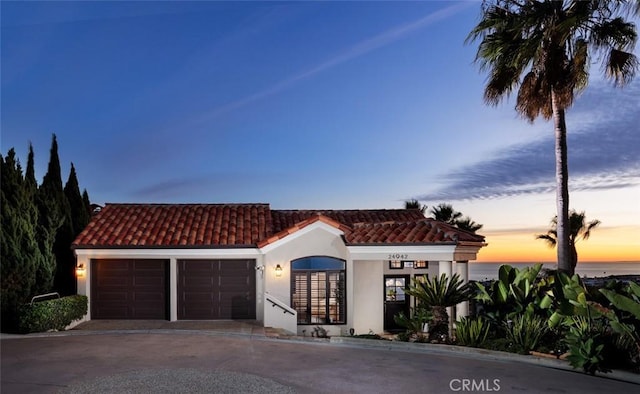mediterranean / spanish home featuring stucco siding, an attached garage, a tiled roof, and driveway