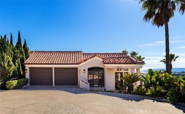 mediterranean / spanish house featuring stucco siding, concrete driveway, an attached garage, and a tiled roof