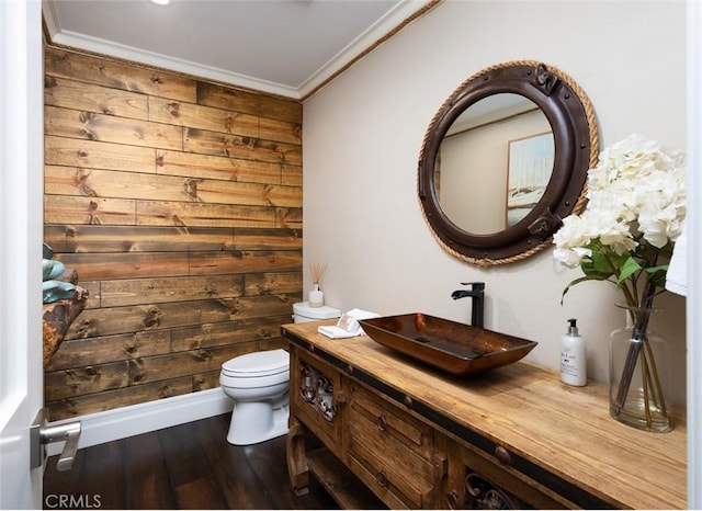 half bathroom with toilet, wood finished floors, vanity, ornamental molding, and wooden walls