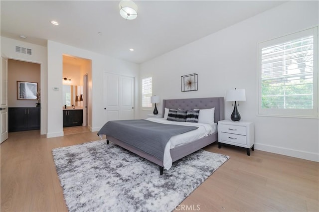 bedroom featuring ensuite bath, light wood-type flooring, visible vents, and baseboards