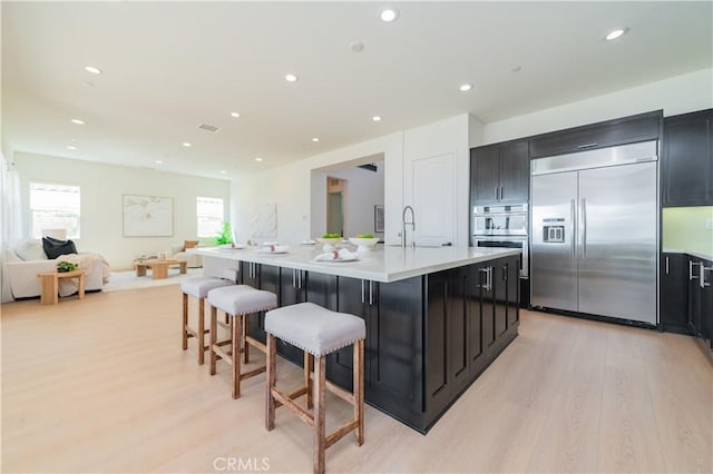 kitchen with light wood-type flooring, light countertops, appliances with stainless steel finishes, and a kitchen bar