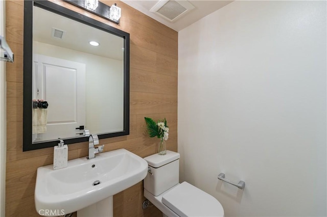 bathroom featuring toilet, visible vents, wooden walls, and a sink