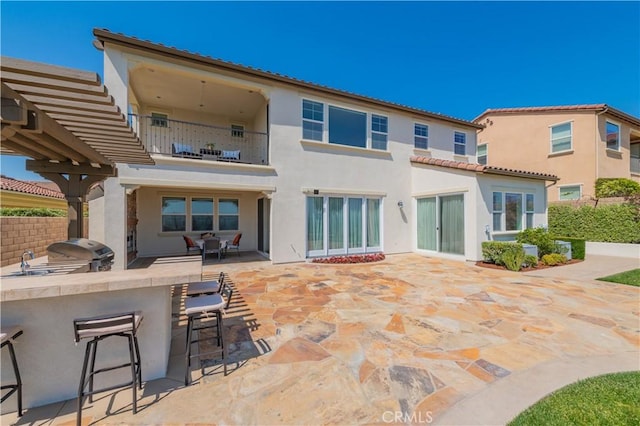 rear view of property featuring a balcony, stucco siding, exterior kitchen, and outdoor wet bar
