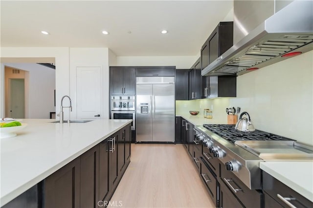 kitchen featuring wall chimney range hood, light countertops, stainless steel appliances, and a sink