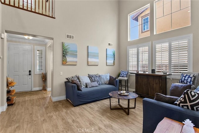 living room with a towering ceiling, baseboards, light wood-style flooring, and visible vents