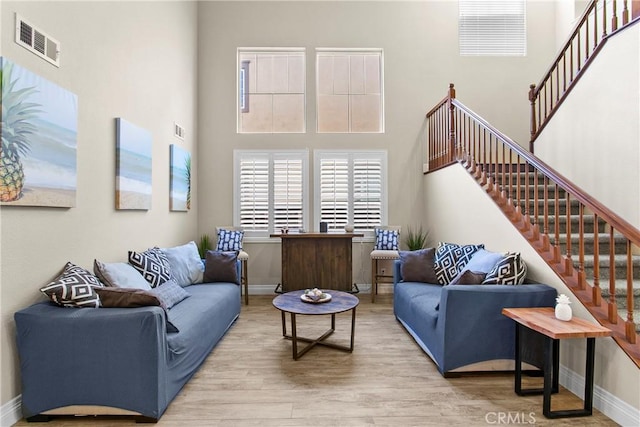 living room with wood finished floors, visible vents, baseboards, a towering ceiling, and stairs