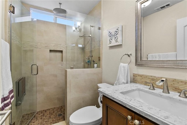 full bathroom featuring toilet, visible vents, a shower stall, vanity, and decorative backsplash