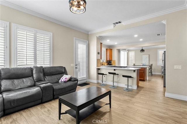 living area featuring crown molding, light wood-style flooring, baseboards, and visible vents