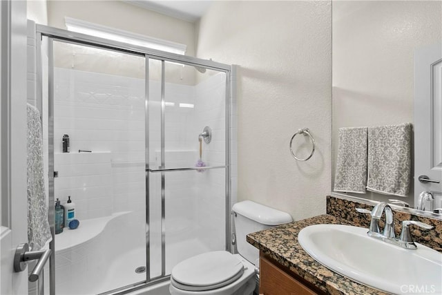 full bathroom featuring vanity, toilet, a stall shower, and a textured wall