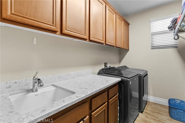 laundry room featuring a sink, cabinet space, washer and clothes dryer, light wood-type flooring, and baseboards