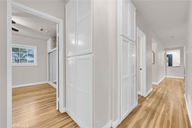 hallway featuring light wood-type flooring, visible vents, and baseboards