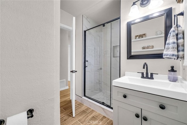 bathroom with wood finished floors, vanity, visible vents, a stall shower, and a textured wall