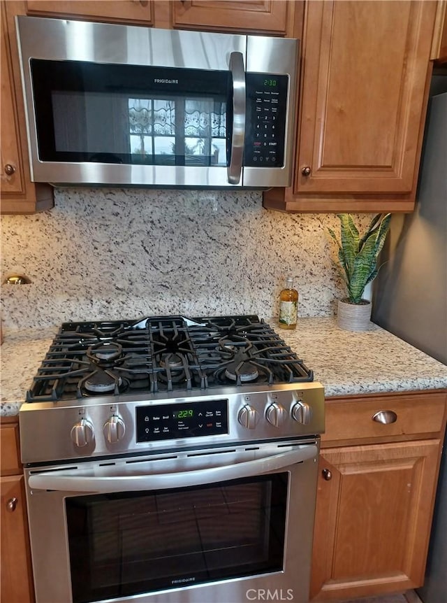kitchen with appliances with stainless steel finishes, decorative backsplash, light stone counters, and brown cabinets