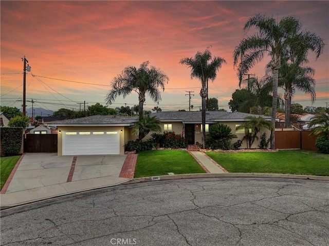view of front facade featuring stucco siding, concrete driveway, a front lawn, and fence