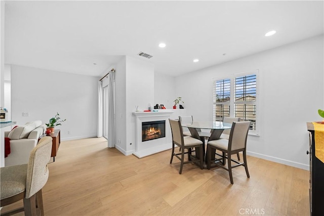 dining room with light wood finished floors, a glass covered fireplace, recessed lighting, and baseboards