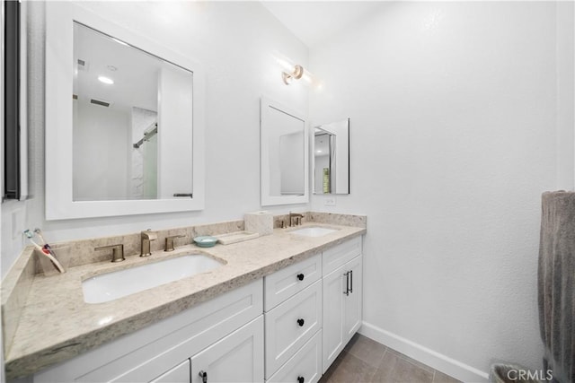bathroom with baseboards, double vanity, and a shower
