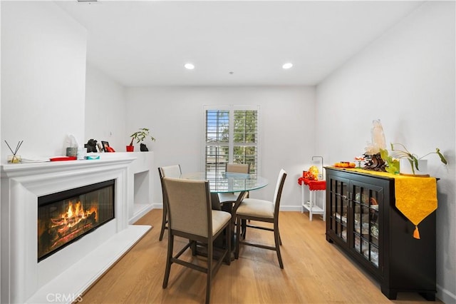dining room featuring wood finished floors, a glass covered fireplace, recessed lighting, and baseboards