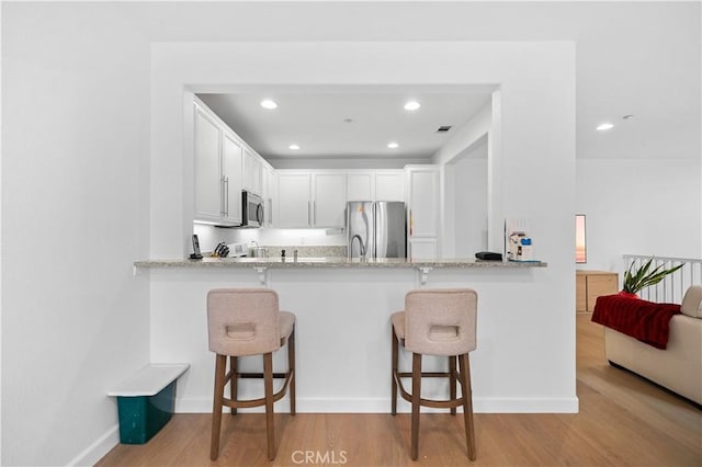 kitchen featuring stainless steel appliances, light wood finished floors, a kitchen breakfast bar, white cabinetry, and recessed lighting
