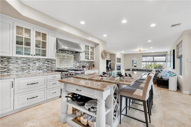 9420 Oak Leaf Dr, Chatsworth, CA 91311 - kitchen with exhaust hood, a breakfast bar, light stone counters, a center island with sink, and tasteful backsplash