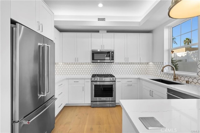 kitchen with a sink, stainless steel appliances, white cabinetry, visible vents, and light stone counters