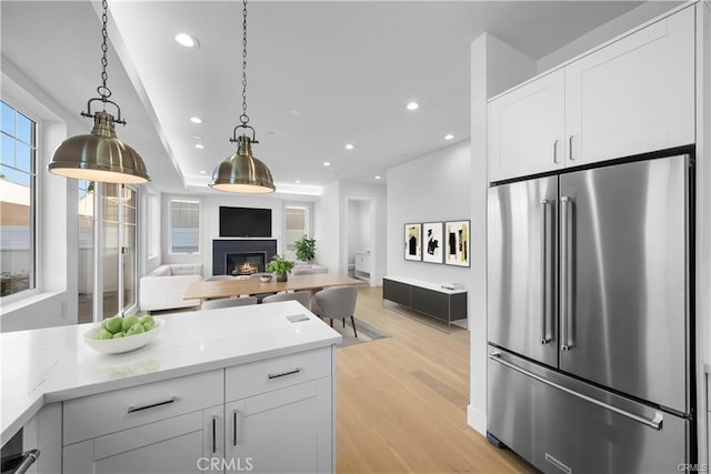 kitchen featuring high end fridge, light wood-style flooring, white cabinetry, open floor plan, and a glass covered fireplace