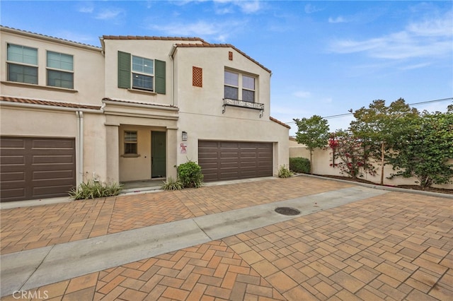 townhome / multi-family property with a tiled roof, an attached garage, stucco siding, and decorative driveway