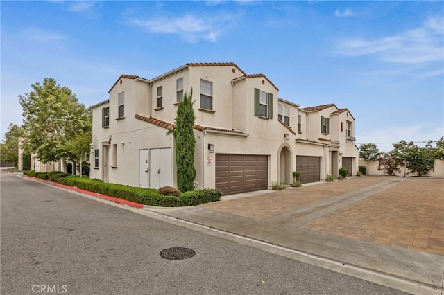view of front of home featuring an attached garage, a residential view, driveway, stucco siding, and a tiled roof
