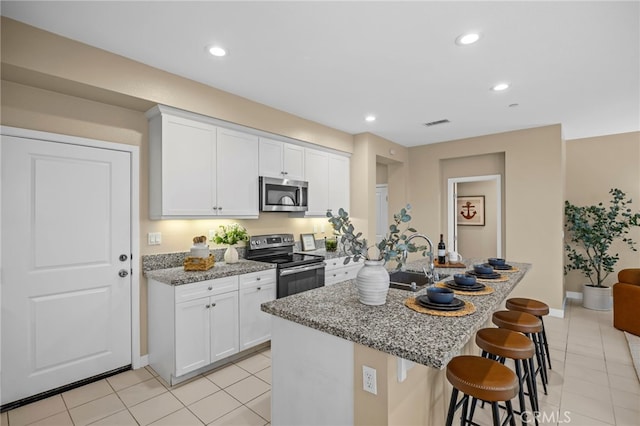 kitchen featuring light tile patterned floors, light stone counters, a sink, a kitchen bar, and appliances with stainless steel finishes