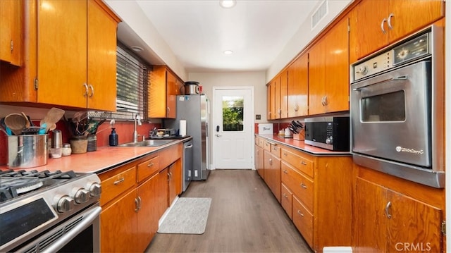 kitchen featuring a sink, brown cabinetry, wood finished floors, visible vents, and appliances with stainless steel finishes