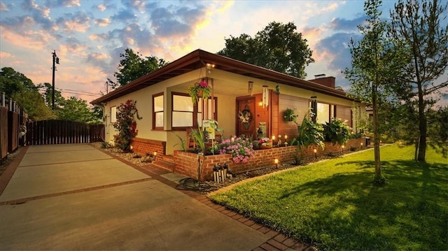 view of front of property featuring a yard, fence, a chimney, and concrete driveway
