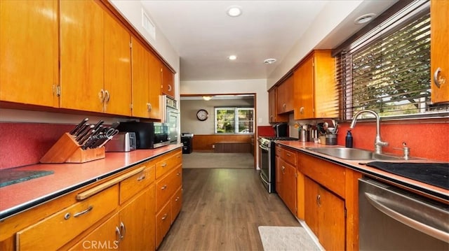 kitchen with wood finished floors, a sink, stainless steel appliances, brown cabinetry, and recessed lighting