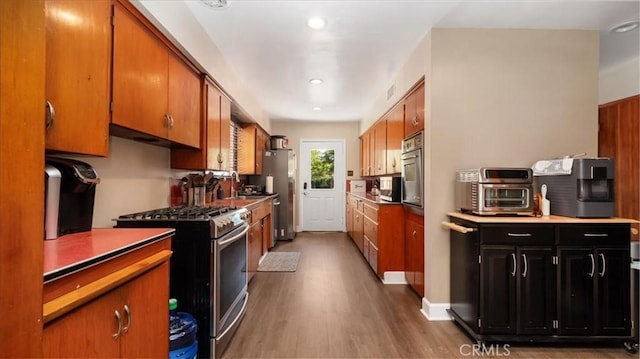 kitchen featuring brown cabinetry, wood finished floors, a toaster, and appliances with stainless steel finishes