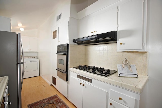 kitchen featuring washer / clothes dryer, under cabinet range hood, a warming drawer, tile counters, and stainless steel appliances