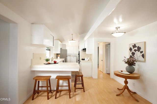 kitchen with a peninsula, a breakfast bar area, freestanding refrigerator, white cabinetry, and light wood-style floors