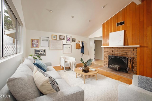 living room featuring lofted ceiling, visible vents, wooden walls, a brick fireplace, and wood finished floors