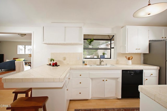 kitchen featuring black dishwasher, a peninsula, light wood-type flooring, and a sink
