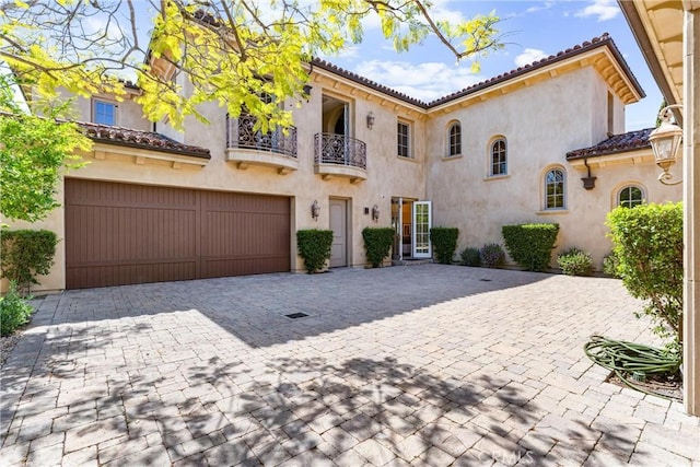 mediterranean / spanish home featuring a garage, stucco siding, decorative driveway, and a balcony