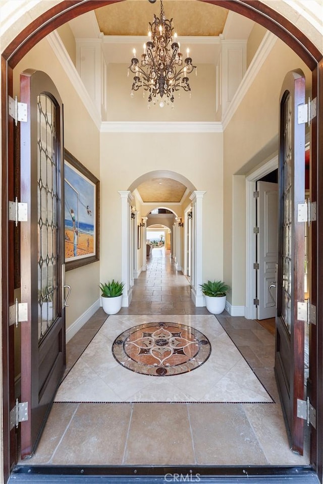 entrance foyer featuring baseboards, ornamental molding, an inviting chandelier, arched walkways, and a high ceiling