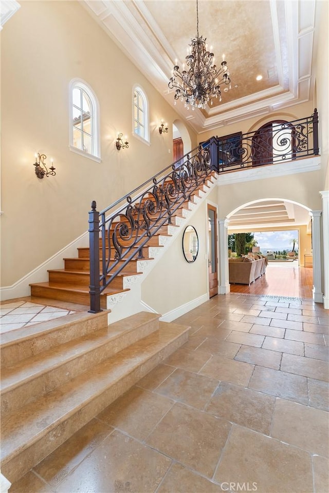 foyer entrance featuring a towering ceiling, arched walkways, a notable chandelier, a raised ceiling, and baseboards
