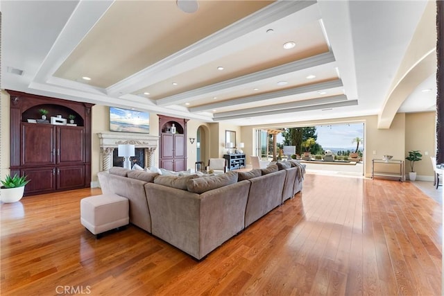 living area featuring light wood finished floors, a tray ceiling, a fireplace, arched walkways, and recessed lighting