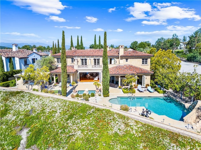 back of house featuring a tiled roof, stucco siding, a chimney, a balcony, and a patio area