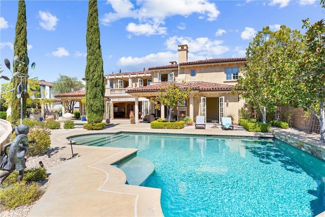back of property with an outdoor pool, a patio, stucco siding, a tiled roof, and a chimney