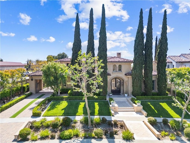 mediterranean / spanish home featuring stucco siding, a tiled roof, a front lawn, and a chimney