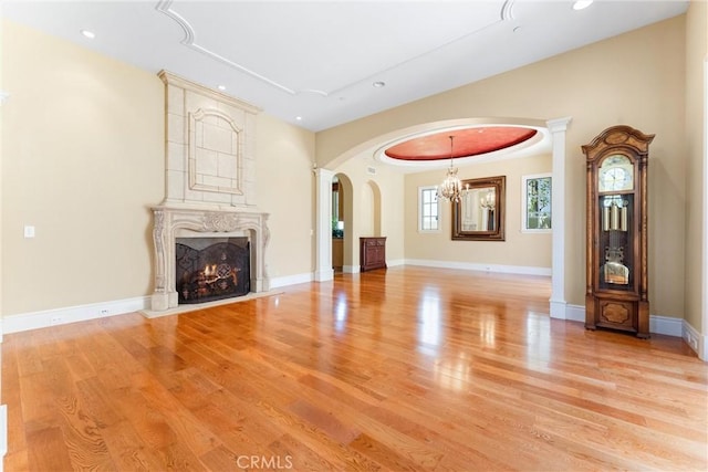 unfurnished living room featuring arched walkways, light wood-style floors, a fireplace, and a chandelier