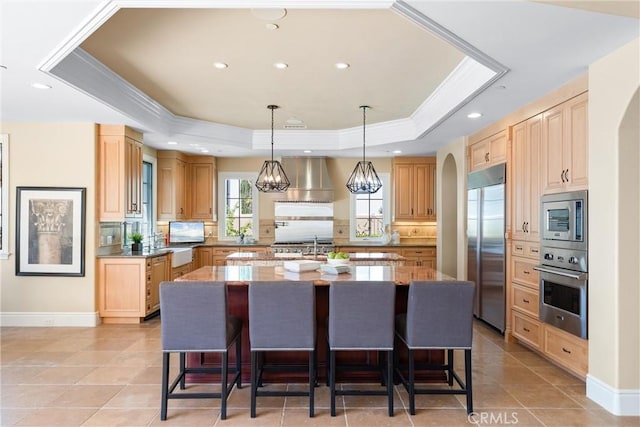 kitchen with an island with sink, built in appliances, a kitchen breakfast bar, and a raised ceiling