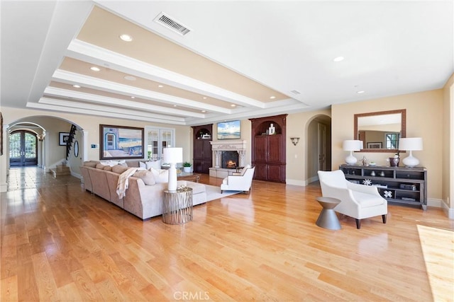 living room with a warm lit fireplace, baseboards, visible vents, arched walkways, and light wood-style floors