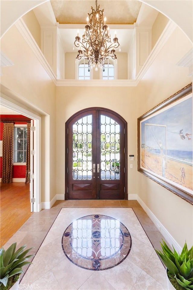entrance foyer with french doors, baseboards, an inviting chandelier, tile patterned floors, and a high ceiling