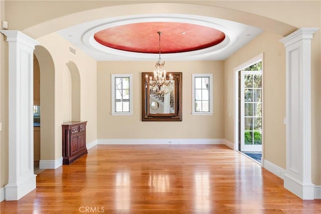 unfurnished dining area with arched walkways, a tray ceiling, and light wood-type flooring